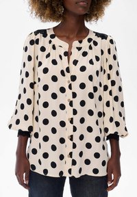 Kremowa bluzka w duże czarne kropki, zapinana na przód, z bąbelkowymi rękawami oraz czarnymi koronkowymi akcentami na ramionach i mankietach.