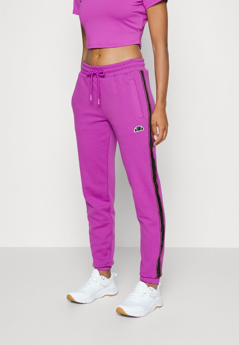 Fuchsia joggers with drawstring waist, side pockets, and black side stripes. Paired with white sneakers, featuring subtle logo accents.