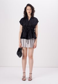 Sort kortærmet top med snøret talje, parret med en lys grå plisseret miniskirt, holder en sort clutch og iført sorte strop sandaler.