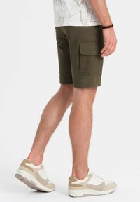 Shorts cargo vert armée avec une poche latérale, présentant une coupe droite. Assortis avec des baskets beige et blanches, mettant en valeur un design texturé.