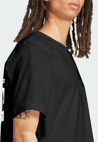 Black short-sleeve t-shirt with a crew neck. Features a graphic print on the front. Material appears smooth with a relaxed fit.