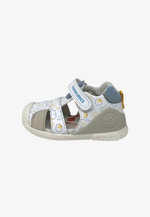 Sandale blanche et grise pour tout-petit avec motifs de dessins animés jaunes et gris, bride velcro étiquetée « biomecanics » et semelle en caoutchouc avec détail du logo.