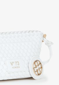 La borsa a tracolla in pelle bianca intrecciata presenta una forma strutturata, un logo impresso, finiture in tonalità oro e un accent di forma rotonda con un design floreale.