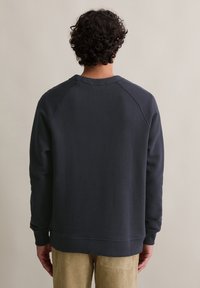 Felpa a girocollo grigio scuro con polsini e orlo a costine, caratterizzata da una vestibilità morbida e maniche raglan. La texture appare morbida e informale.