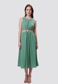 Vestido verde sin mangas con un corte redondo en la cintura, tela texturizada y una falda fluida que llega a la mitad de la pantorrilla.