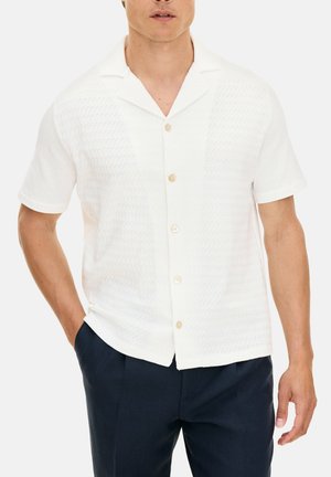 Korte mouwen witte shirt met een gestructureerd ontwerp, voorzien van een kraag en lichtbruine knopen, gecombineerd met donkerblauwe broeken.