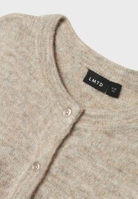 Beige stickad cardigan med rund halsringning, med en rad av tre ljusa knappar och en etikett med "LMTD" och storlekinformation.