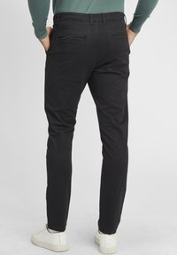 Zwarte katoenen broeken met een slim fit, voorzien van twee achterzakken en gedragen met witte sneakers. Glad van textuur en een strakke uitstraling.