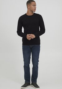 Czarny sweter dzianinowy z okrągłym dekoltem, połączony z niebieskimi dżinsami i czarnymi trampkami z białymi podeszwami. Minimalistyczny design, brak widocznych wzorów.