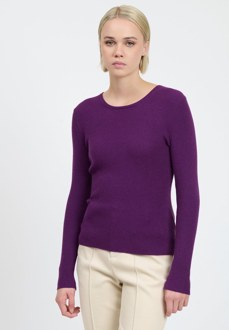 Lila gerippter Strickpullover mit langen Ärmeln und rundem Halsausschnitt, kombiniert mit cremefarbenen Hosen. Glatte Textur und taillierter Schnitt.