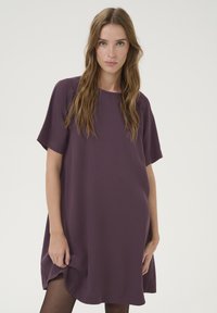 Robe ample à manches courtes en tissu violet profond. Texture lisse avec un col rond et de légentes fentes sur les côtés à l'ourlet.