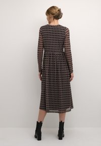 Långärmad midi-klänning i mönstrad genomskinlig tyg med svarta, bruna och krämfärgade geometriska mönster; elastisk midja, flödande passform och mjuk textur.