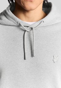 Felpa grigia realizzata in tessuto morbido, con cappuccio regolabile e logo ricamato sul petto. Texture liscia e design informale.