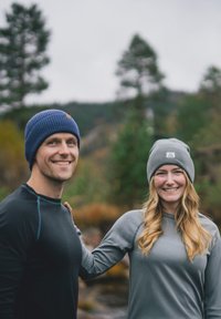 Two people outdoors wearing beanies; one blue, one gray. They are dressed in long-sleeve athletic tops, against a blurred natural background.