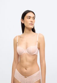 Pirosító rózsaszín csipkés melltartó hullámos széllel és geometriai mintákkal, hozzáillő csipkés bugyival. Állítható pántok és finom fém díszítések.