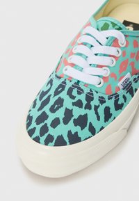 Turquoise alapú vászon sportcipő leopárdmintával feketében és korallban, fehér fűzőkkel és textúrált krémszínű gumitalppal.