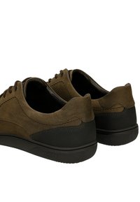 Hnědé semišové boty s černou gumovou podrážkou, viděné ze zadu. Šňůrky jsou zavázané, což ukazuje na elegantní design.