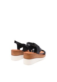 Sandali con zeppa in pelle nera caratterizzati da un design con cinturini incrociati, fibbia regolabile e una suola piattaforma bianca a contrasto con una base marrone.