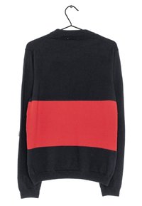 Svart tröja med ett rött horisontellt rand över mitten. Har en hög halsringning och långa ärmar. Tillverkad av ett mjukt, texturerat tyg.