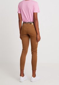 Bruna cargobyxor med slim fit, som har en bakficka och ett bälte. Matcher med en ljusrosa t-shirt och vita sneakers.