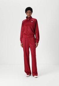 Red, satin athletic tracksuit with a zip-up jacket and elastic waistband pants. Features white accents and a logo on the jacket.
