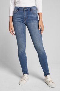 Chude niebieskie dżinsy z pięcioma kieszeniami, z zapięciem na guzik i lekkim przetarciem. Połączone z białymi trampkami.