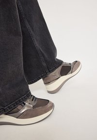 Grå läder- och tygsneakers med en tjock vit sula, med snörning och kontrasterande svarta nätinslag. Bärs med mörka jeans.