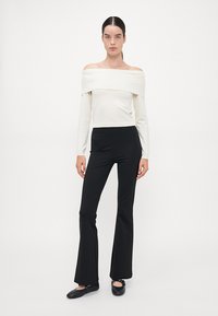 Hvit av-shoulder langermet topp parret med svarte vidde bukser, laget av mykt stoff med en jevn tekstur og tettsittende design.