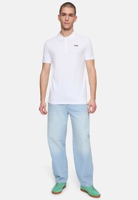 Valkoinen polo-paita, jossa on kaulus ja lyhyet hihat, ja jossa on pieni Fila-logo vasemmassa rinnassa. Yhdistetty vaaleansinisiin farkkuihin ja vihreisiin kenkiin.