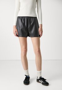 Svarta skinnshorts med elastisk midja, slät textur och lös passform. Matchade med svarta sneakers och vita ankelsockor.