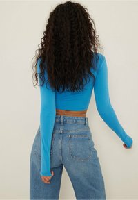 Crop top blu a maniche lunghe con una texture liscia, abbinato a jeans chiari a vita alta con tasche posteriori e un fit rilassato.