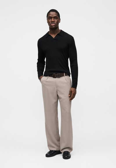 Polo noir à manches longues côtelé avec un col plat, associé à un pantalon beige clair ajusté et des chaussures noires. Design épuré et élégant.