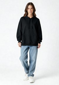 Felpa nera con cappuccio, tasca a marsupio, polsini e orlo a costine, abbinata a jeans azzurri a vestibilità comoda e sneakers bianche.