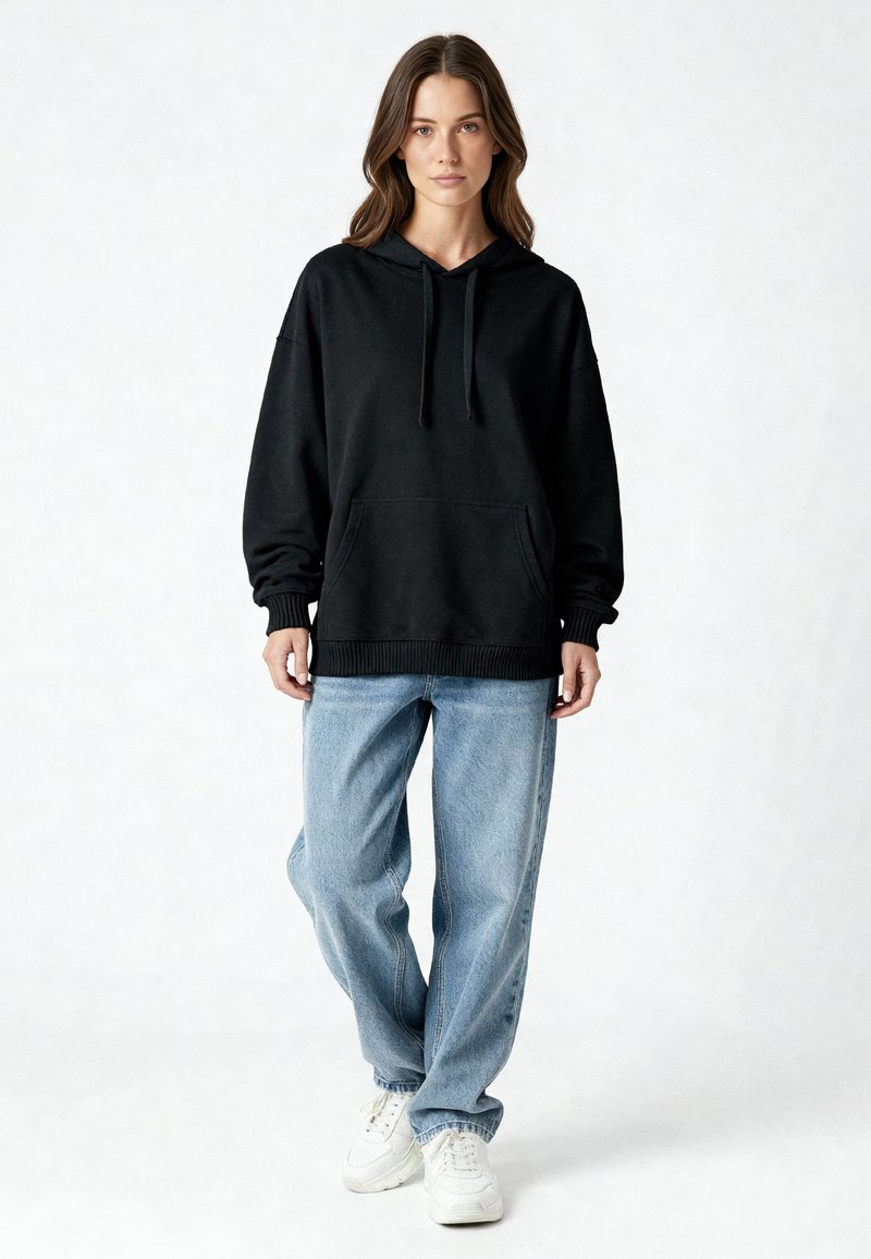 Felpa nera con cappuccio, tasca a marsupio, polsini e orlo a costine, abbinata a jeans azzurri a vestibilità comoda e sneakers bianche.
