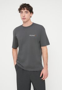 Γκρι βαμβακερό μπλουζάκι με στρογγυλή λαιμόκοψη, κοντά μανίκια και μικρό λευκό και πορτοκαλί λογότυπο "McLaren" στο αριστερό στήθος.