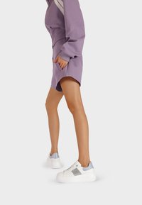 Sneakers bianchi con una suola spessa, dettagli blu e un particolare scintillante di lato. Indossati con un vestito viola dotato di tasche.