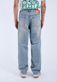 Ljusblå denimjeans med avslappnad passform, som har två bakfickor och en brun etikett vid midjan, visad bakifrån.