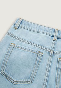 Détail d’un jean en denim bleu clair montrant la poche arrière, les passants de ceinture et les coutures orange visibles sur un fond clair uni.