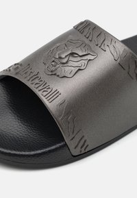 Szare klapki z teksturowanym wierzchem z emblematem lwa i wytłoczonym logo, osadzone na czarnej, teksturowanej podeszwie.