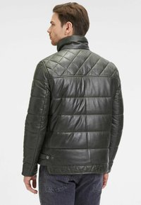 Giacca in pelle verde scuro con un design trapuntato, caratterizzata da un collo rialzato e dettagli testurizzati a contrasto lungo il retro e i lati.