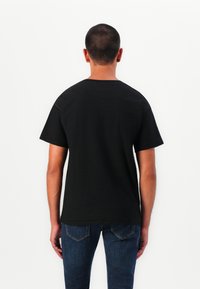 T-shirt noir à manches courtes en coton, avec un col rond et une coupe décontractée, montré de dos avec un jean en denim bleu.