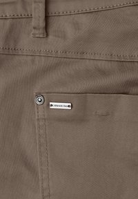Tissu marron en gros plan d'une poche de pantalon avec un bouton en métal et une étiquette de marque "Street One" fixée près de la couture.
