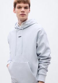 Ανοιχτό μπλε φούτερ με κουκούλα από λείο ύφασμα, με μπροστινή τσέπη και μαύρο λογότυπο "BOSS" στο κέντρο του στήθους. Κορδόνια στη κουκούλα.