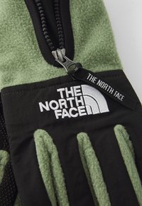 Zöld és fekete polárdzseki fekete cipzárral, a mellel elhelyezett zsebben fehér hímzéssel, rajta: "THE NORTH FACE".