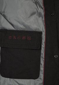 Černá bunda se šedou podšívkou a kapsou, na které jsou vyšitá symboly péče o prádlo v červené barvě. Hladký povrch, zapínání na knoflík.