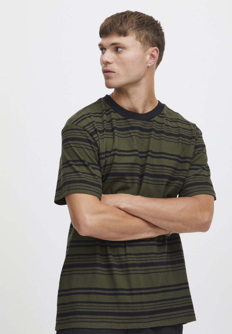 Camiseta de rayas verde olivo con rayas horizontales negras, de mangas cortas y con un cuello de canalé negro. Tejido suave con un corte relajado.