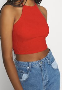 Top corto a coste rosso con design a collare. Indossato con jeans alti in denim blu chiaro con tasche e dettagli cuciti.