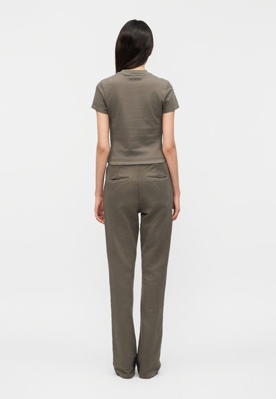 Γυναίκα με μακριά σκούρα μαλλιά που φορά στενή πράσινη κοντομάνικη μπλούζα και ταιριαστό παντελόνι ψηλής μέσης, όρθια με την πλάτη στραμμένη.