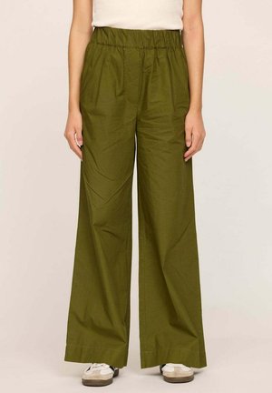 Pantalons larges en vert olive avec une taille élastique, présentant une texture lisse et des poches latérales, accompagnés de baskets blanches.