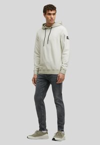 Light gray hooded sweatshirt with drawstrings, ribbed cuffs and hem, worn with dark gray slim-fit jeans and beige athletic shoes.